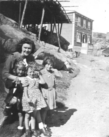 070: Cede McCarthy with three young pupils. l-r Mary Ennis, Betty Whelan,  Rosemary Whelan. (circa 1944) Tom Rose's house is in the background; Pat Lambe's  flake is at left; the road up Lambe's hill is between the flake and the house;  the 'gallus' is in the center.  - Mary daughter of Vincent Ennis &amp;amp; Min Carroll; Betty and Rosemary daughters of William  Whelan &amp;amp; Mary Bridget Carroll